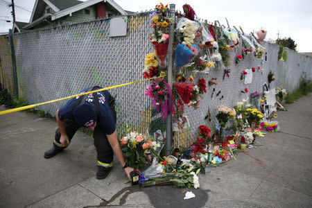 A firefighter picks up a fallen bottle of whiskey at a sidewalk memorial near the burned warehouse following the fatal fire in the Fruitvale district of Oakland, California, U.S. December 5, 2016. REUTERS/Lucy Nicholson