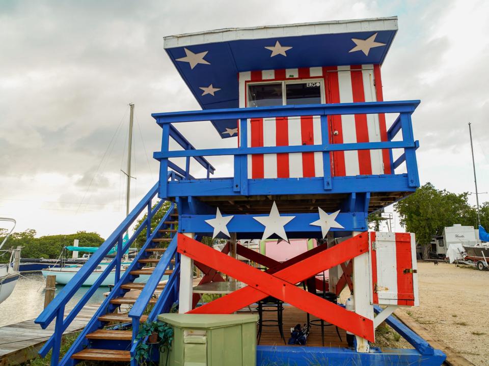 The lifeguard tower is red white and blue on a cloudy day