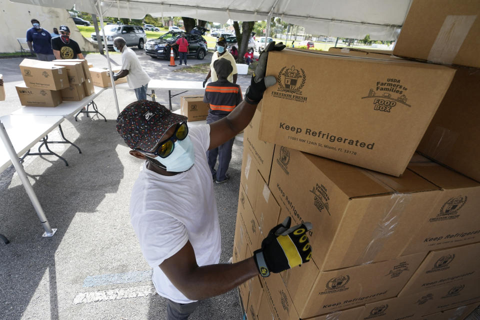 FILE - In this Oct. 6, 2020, file photo, city worker Randy Greice, foreground, unloads a pallet of food at a food distribution event in Opa-locka, Fla. President-elect Joe Biden will inherit a mangled U.S. economy, one that never fully healed from the coronavirus and could suffer again as new infections are climbing. The once robust recovery has shown signs of gasping after federal aid lapsed. Ten million remain jobless and more layoffs are becoming permanent. The Federal Reserve found that factory output dropped. (AP Photo/Wilfredo Lee, File)