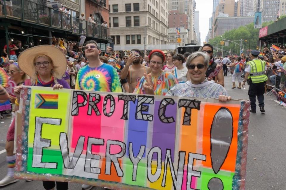 A family at New York Pride is holding up a banner that says "Protect Everyone!"