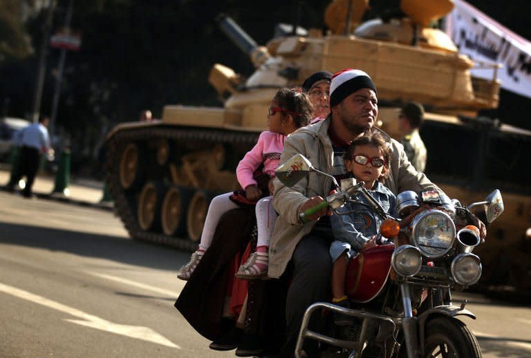 An Egyptian family rides a motorbike past a tank outside the presidential palace in Cairo. Egypt's powerful military has demanded the Islamist-led government and political foes start dialogue and warned it will not permit events to take a "disastrous" turn