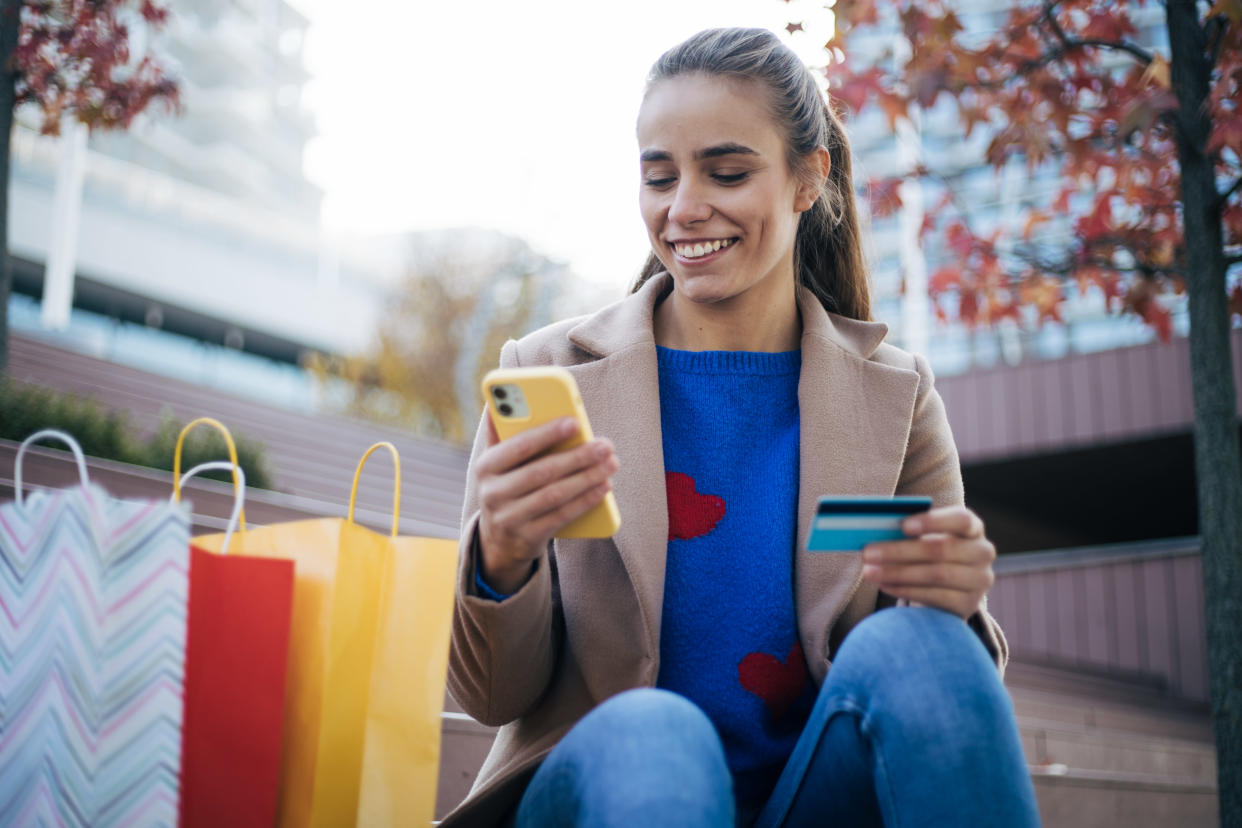 Young woman with bags nearby shops from her phone. 