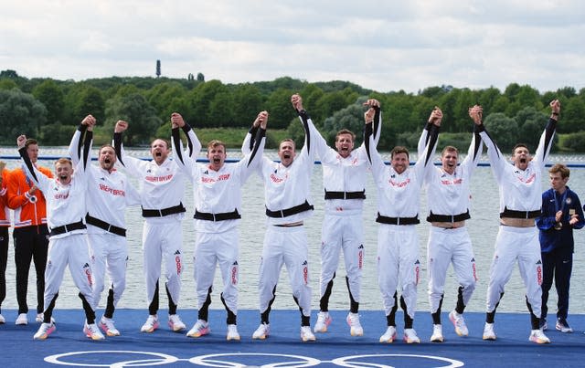 Great Britain’s men's eight in a line, holding hands up in the air and cheering. 