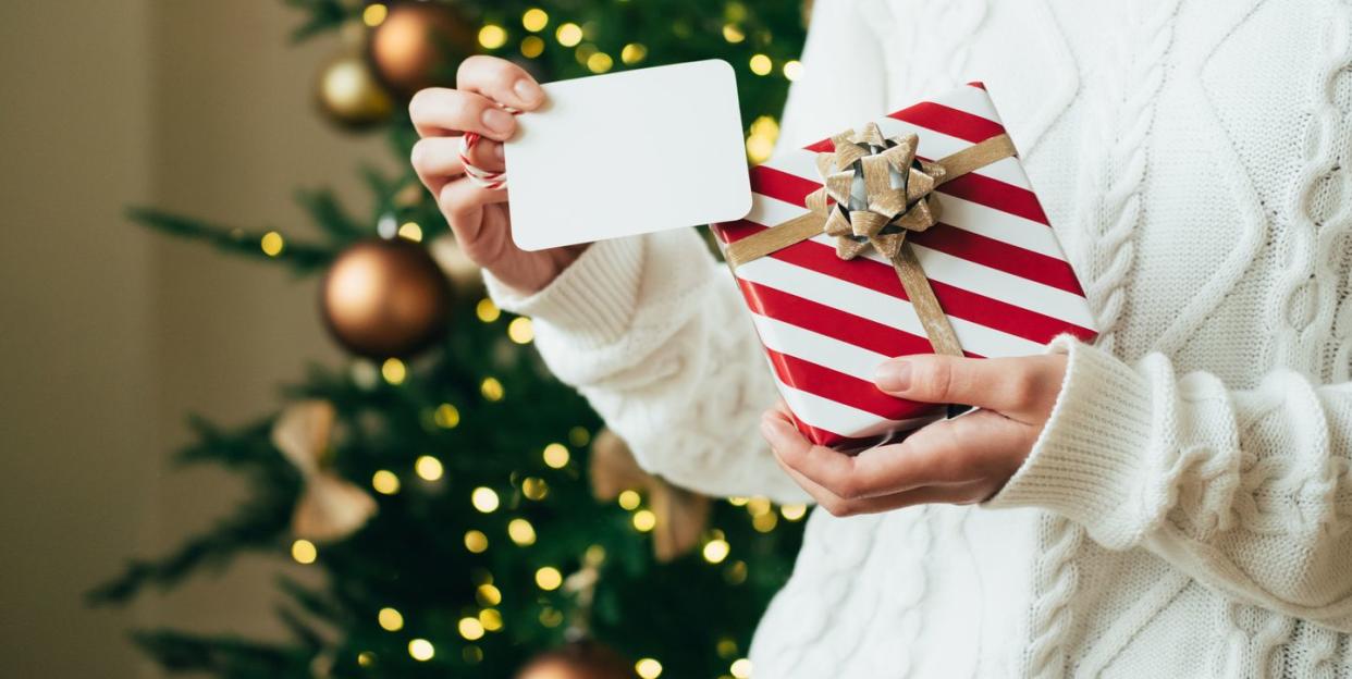 woman in white sweater is holding red white gift box