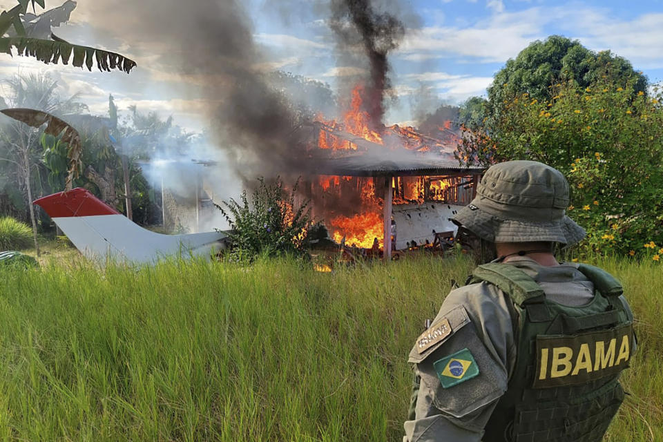 In this image provided by IBAMA, Brazil's Environmental Agency, an agent watches as a structure and plane belonging to miners is engulfed in flames in the Yanomami Indigenous territory, Roraima state, Brazil, Feb. 6, 2023. Brazilian authorities launched an operation to reclaim Yanomami Indigenous territory from thousands of illegal gold miners who have contaminated rivers and brought famine and disease to one of the most isolated populations of the world. (IBAMA via AP)