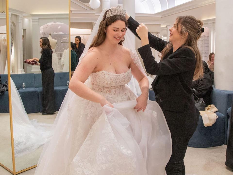 A bridal consultant puts a tiara on a woman wearing a strapless wedding dress.