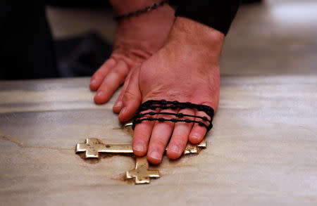 A worshipper, holding a rosary, touches a cross in one of the 28 marble steps of the Holy Stairs in Rome, Italy April 16 2019. REUTERS/Remo Casilli