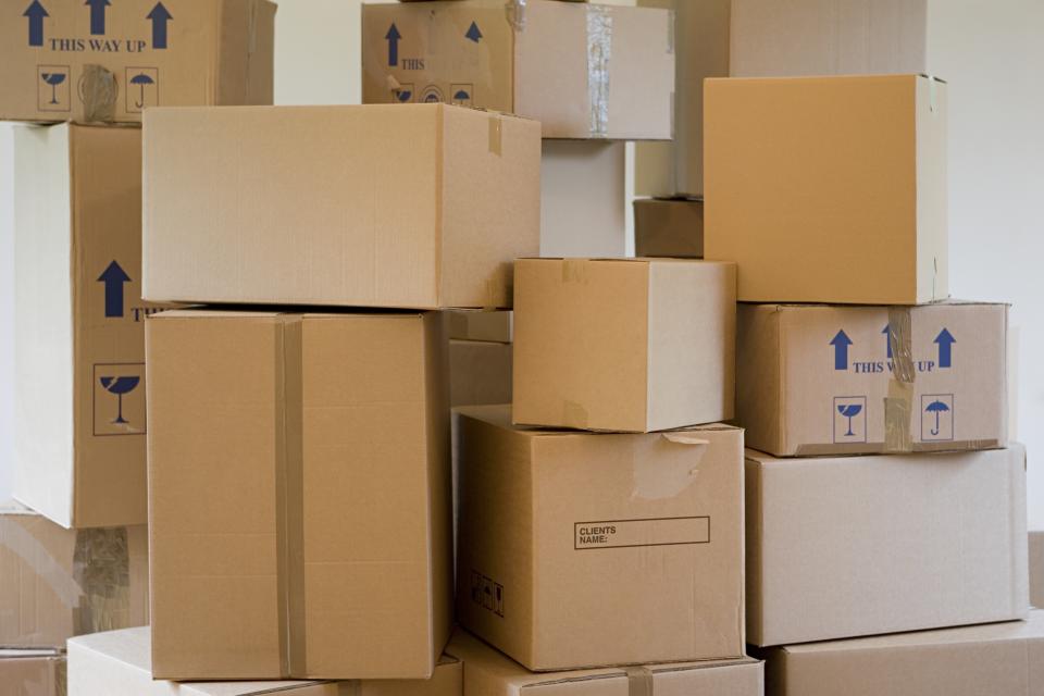 Stacked cardboard moving boxes in various sizes, some labeled with "This way up" and fragile symbols