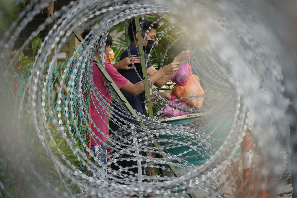 Residents receive food from a delivery man through barbwire at Segambut Dalam area placed under the enhanced movement control order (EMCO) due to drastic increase in the number of COVID-19 cases recorded in Kuala Lumpur, Malaysia, Sunday, July 4, 2021. Malaysia starts further tightening movement curbs and imposes a curfew in most areas in its richest state Selangor and parts of Kuala Lumpur, where coronavirus cases remain high despite a national lockdown last month. (AP Photo/Vincent Thian)