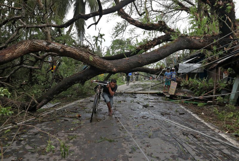 A man walks with his bicycle under an uprooted tree after Cyclone Amphan made its landfall, in South 24 Parganas district