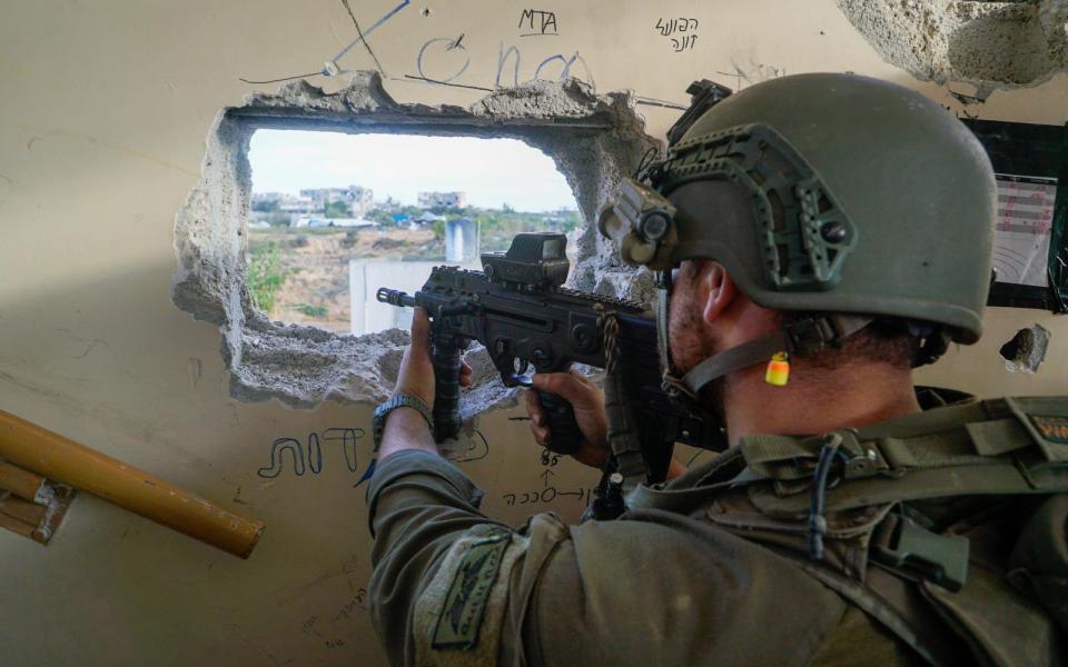 A soldier aims his gun through a hole in a wall in Gaza