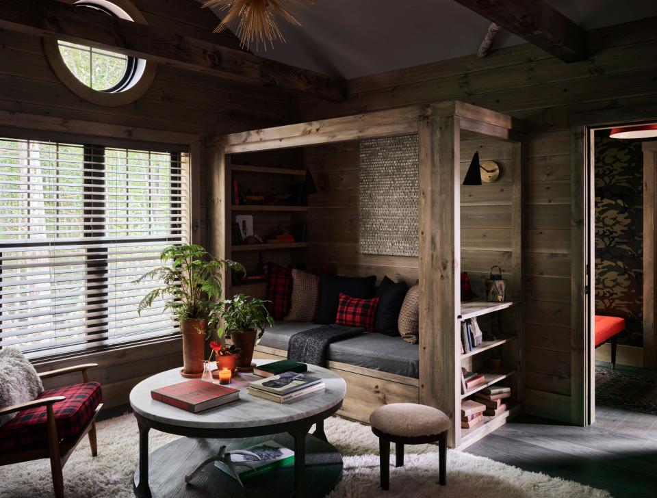 The foyer opens to a cozy living room featuring a shag rug, midcentury chairs with cushions in L.L. Bean’s signature red-and-black plaid, and a daybed and pillows done in men’s suiting fabrics, including gray flannel and tweed.