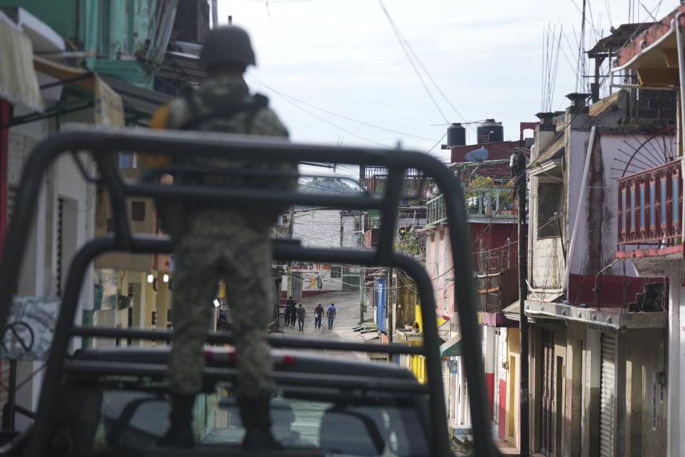 Agricultores pasan junto a tiendas cerradas para trabajar en el campo bajo la vigilancia de soldados en Tila, en el estado de Chiapas, México,el martes 18 de junio de 2024. La población se está marchando de la localidad debido a la violencia relacionada con el crimen organizado. (AP Foto/Fernando Llano)