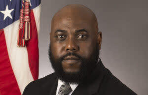 A man in a suit standing in front of a flag.