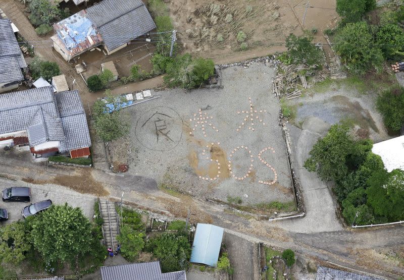 An aerial view shows the words "Rice, Water, SOS" spelled out on the ground in the flood-ravaged Kuma village