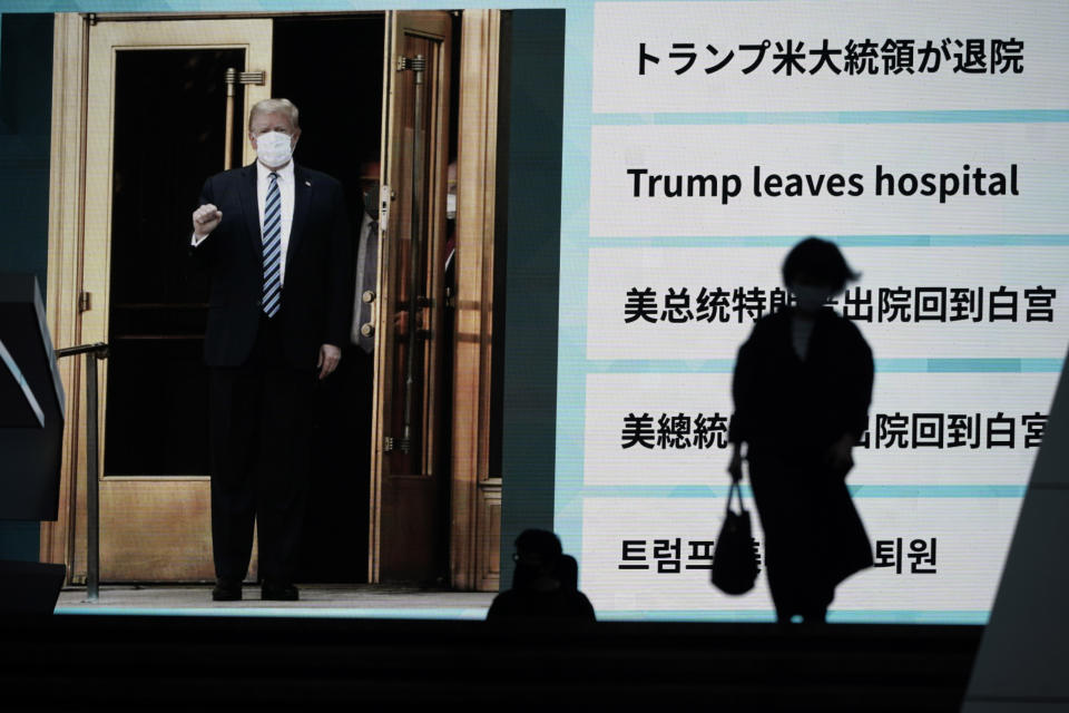 People walk past a screen showing the news report that President Donald Trump has left a hospital to return to the White House after receiving treatments for COVID-19, Tuesday, Oct. 6, 2020, in Tokyo. (AP Photo/Eugene Hoshiko)