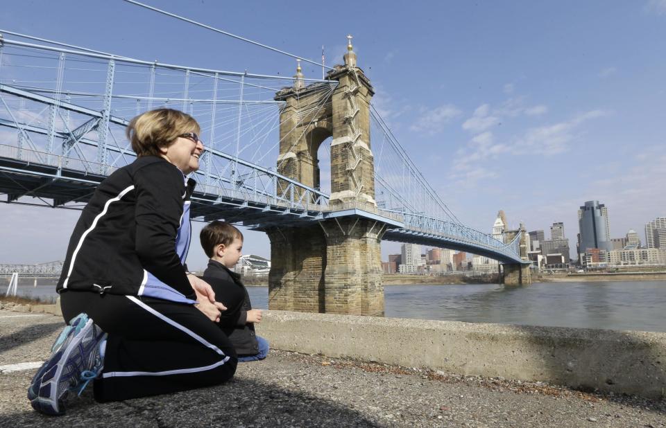 This April 9, 2013 photo shows Yvonne Parmley kneeling with her grandson, Finley MacKay, as they look towards downtown Cincinnati next to the Roebling Suspension Bridge over the Ohio River in Covington, Ky. The bridge was the model for New York City's Brooklyn Bridge. (AP Photo/Al Behrman)