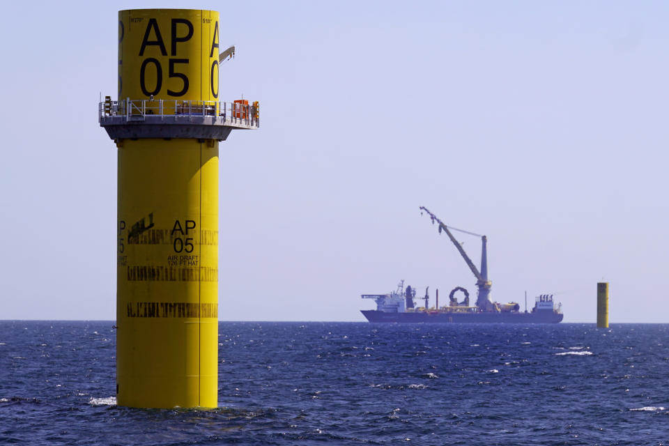 A monopile, left, sits above the waterline awaiting its tower, blades and turbine sections, Tuesday, July 11, 2023, off the coast of Rhode Island. The trade association that represents the offshore service industry is going to great lengths to make sure that jobs go to Americans as the U.S. offshore wind industry ramps up. At rear is the crane ship Bokalift 2, flagged in Cyprus, with a monopile resting on its deck. (AP Photo/Charles Krupa)