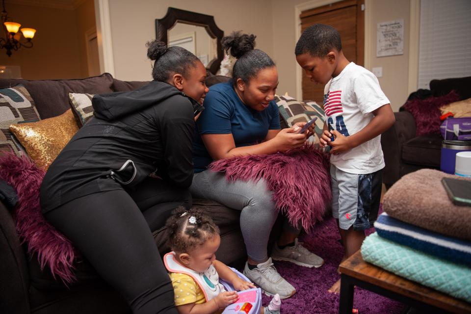 Three kids surround a woman on a couch as she watches a cellphone video.