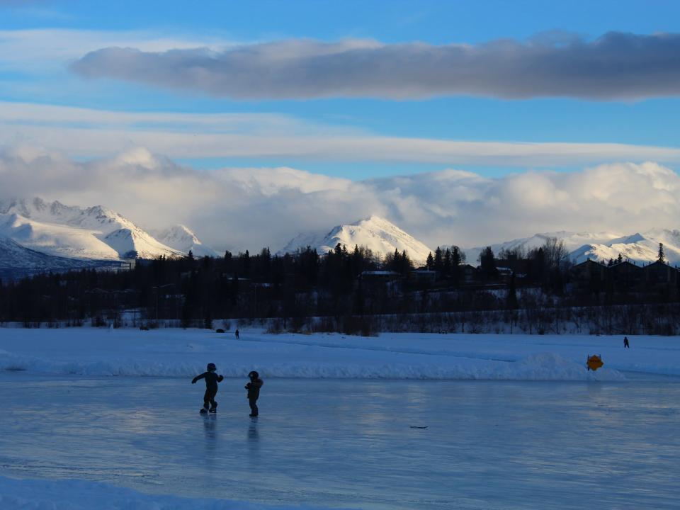 Kids skating on a frozen lake with mountains directly in the background