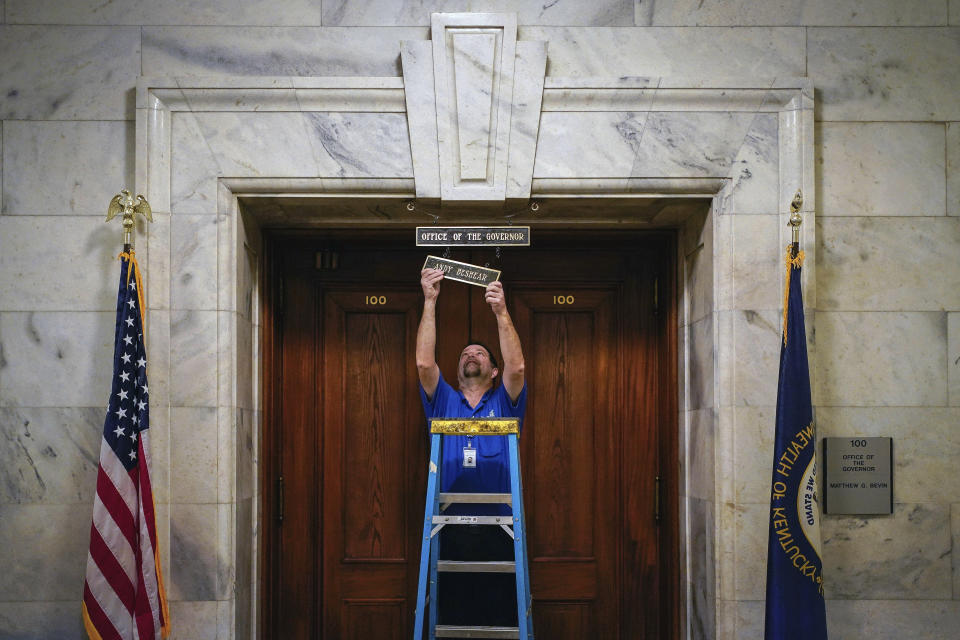Joel Benowit, operations branch manager for finance facilities, hangs a name plaque for Kentucky's Democratic Gov. Andy Beshear over the Governor's Office in the Capitol Building shortly after his private swearing-in ceremony, early Tuesday, Dec. 10, 2019, in Frankfort, Ky. (Bryan Woolston/Pool Photo via AP)