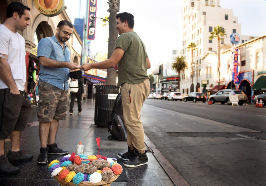 Andrew Coronel, center, sells a keychain to Gopal Lalwani, second from left, with Carmine Giordano, at left, both visiting from the East Coast, on Hollywood Boulevard, Nov. 7, 2017. (Credit: Christina House / Los Angeles Times)