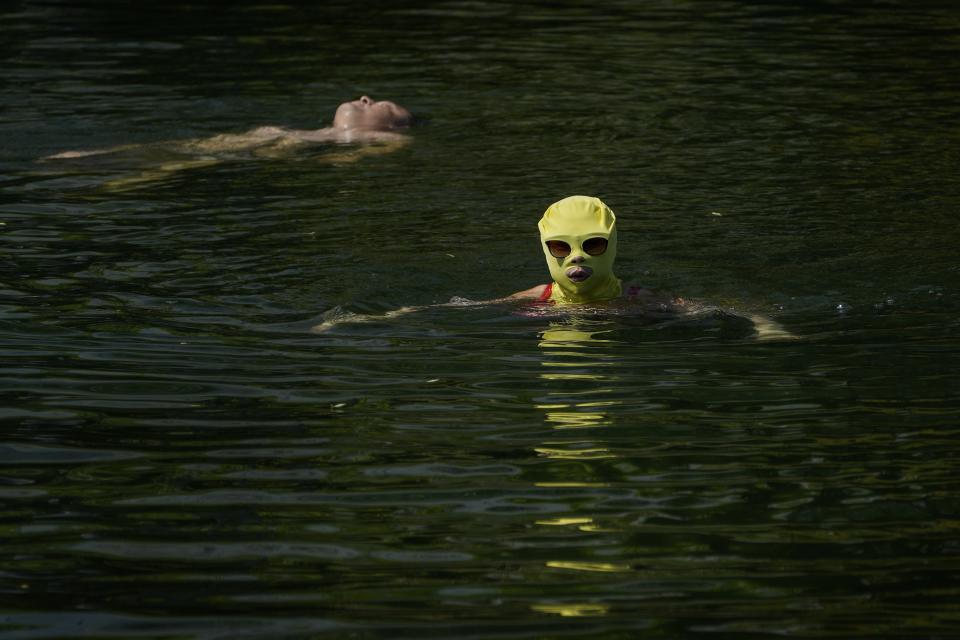 FILE - A woman wearing sun protection headgear and sunglasses swims as residents cool off on a sweltering day at an urban waterway in Beijing, July 10, 2023. Climate change is making heat waves crawl slower across the globe and last longer with higher temperatures over larger areas, a new study finds. (AP Photo/Andy Wong, File)