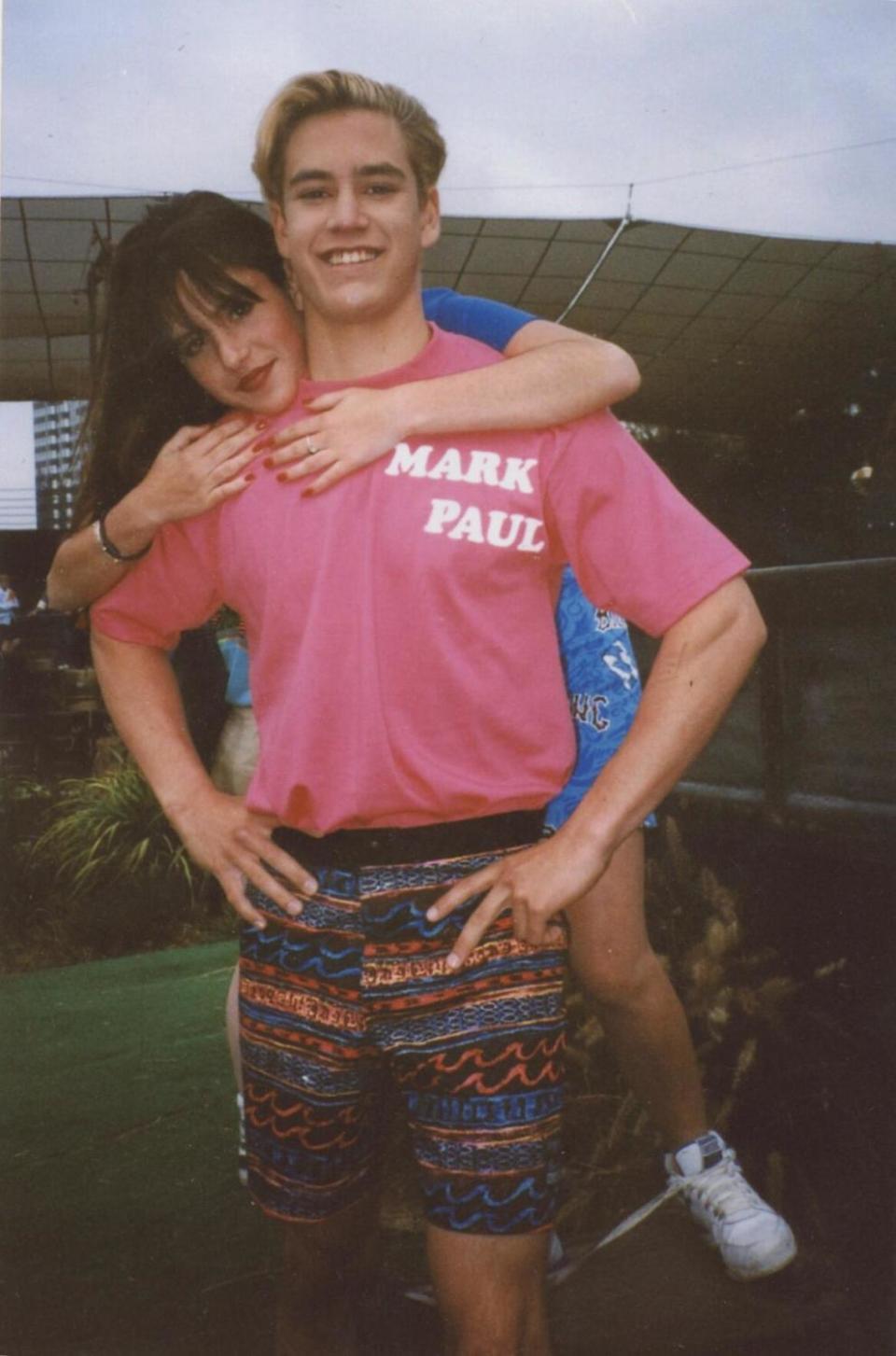 A girl in a blue shirt climbing on the back of a boy in a pink shirt reading Mark Paul