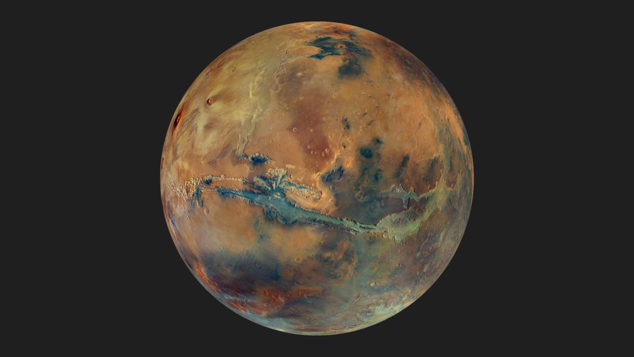  a mostly red planet with shades of blue and green speckled throughout 