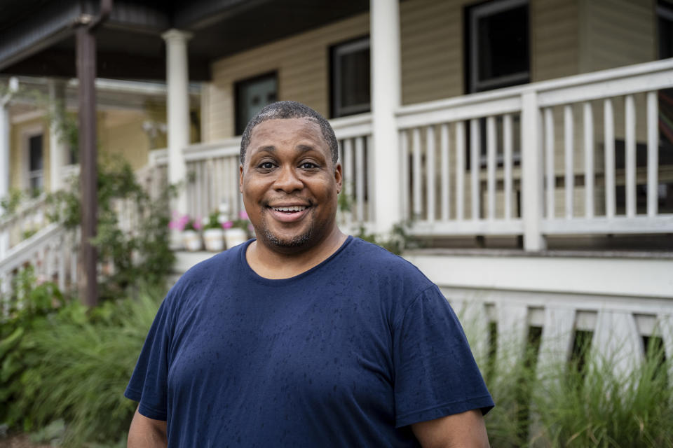 Man in a casual shirt smiling in front of a house with a porch