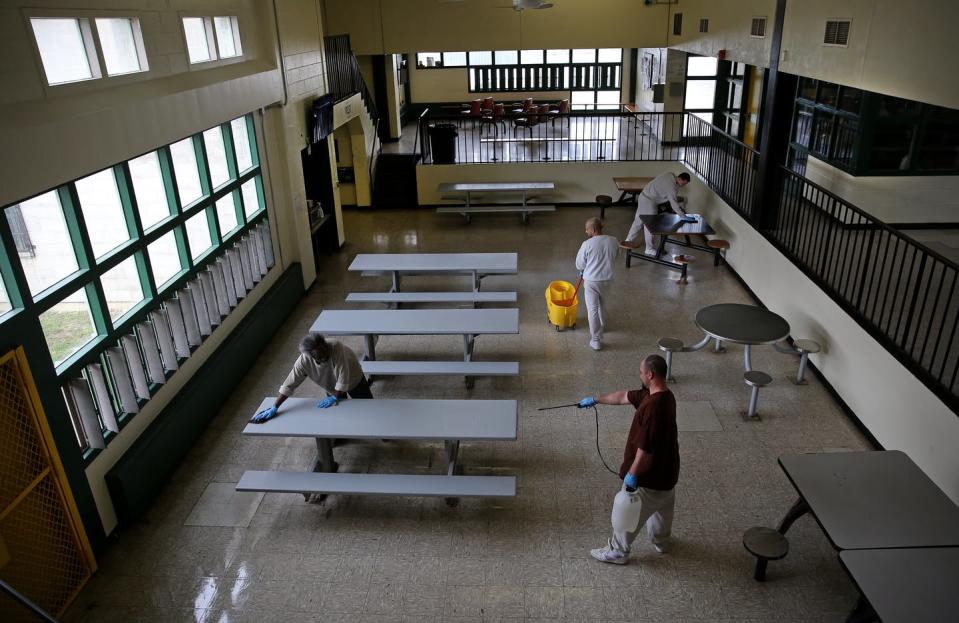 People clean and spray a room with picnic tables and seats.