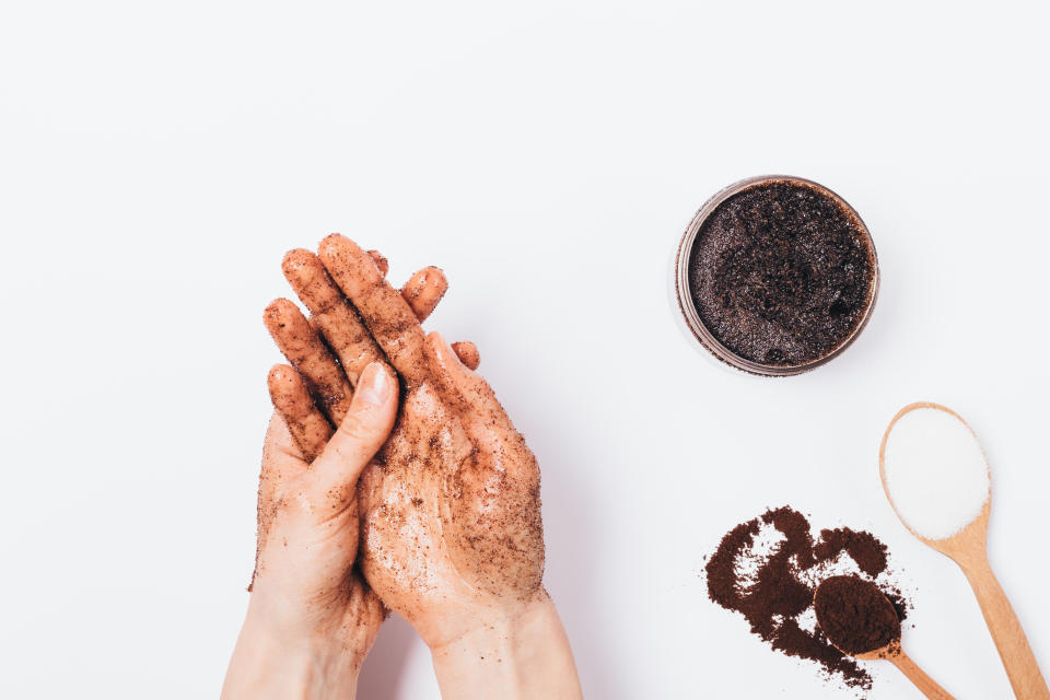 Young woman's hands apply massaging moves homemade cosmetic scrub of fresh ground coffee, sugar and coconut oil, top view on white table.