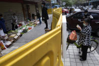 A resident wearing a mask to protect against the spread of the coronavirus checks her purchase after buying groceries from vendor across barriers used to seal off a neighborhood in Wuhan, China, Friday, April 3, 2020. Sidewalk vendors wearing face masks and gloves sold pork, tomatoes, carrots and other vegetables to shoppers Friday in the Chinese city where the coronavirus pandemic began as workers prepared for a national memorial this weekend for health workers and others who died in the outbreak. (AP Photo/Ng Han Guan)