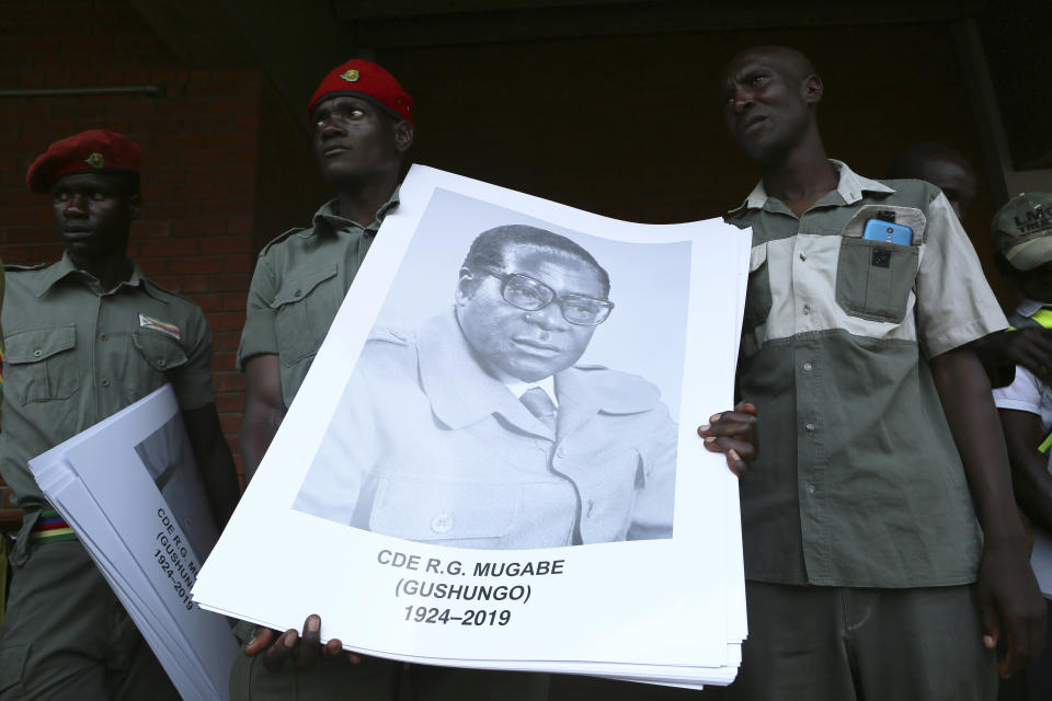 Supporters the late former Zimbabwean leader, Robert Mugabe hold up his portrait as his remains arrive at the National Sports stadium during a funeral procession in Harare, Saturday, Sept, 14, 2019. African heads of state and envoys are gathering to attend a state funeral for Mugabe, whose burial has been delayed for at least a month until a special mausoleum can be built for his remains. (AP Photo/Tsvangirayi Mukwazhi)