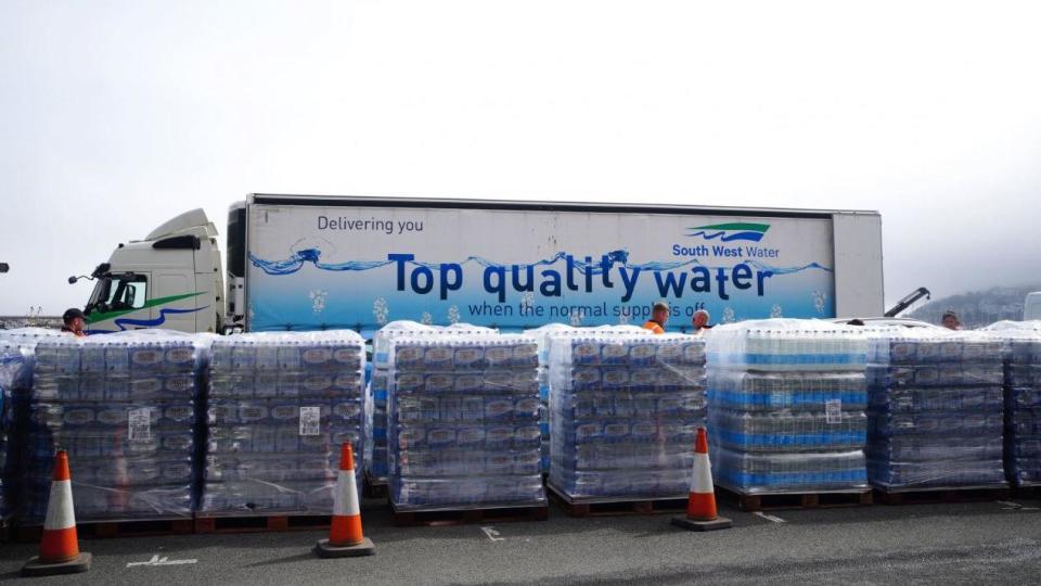 Pallets of bottled water in front of a South West Water lorry that says "top quality water"