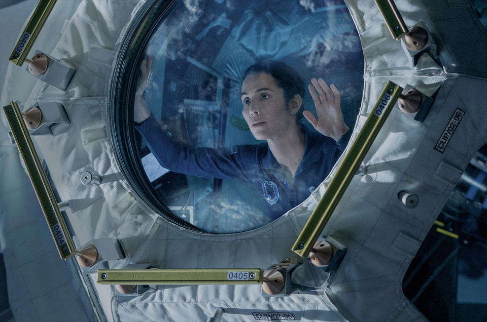 a woman in a blue flight suit looks out a circular window