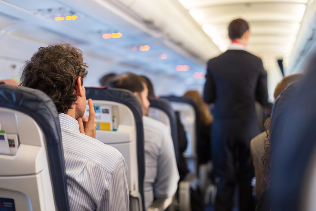 passengers seated on the airplane with flight attendant going down the aisle