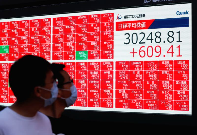 Men wearing protective face masks amid the coronavirus disease (COVID-19) outbreak look at an electronic board displaying Japan's Nikkei Index outside a brokerage in Tokyo