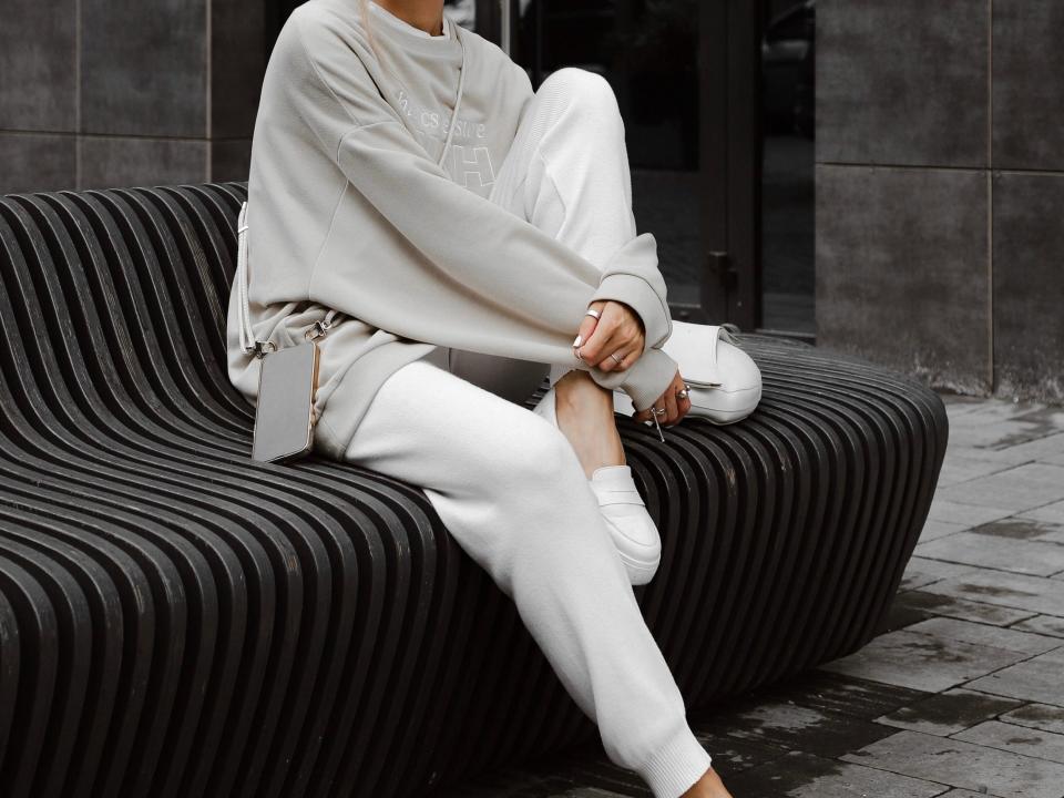 person posing on a bench wearing a neutral colored tracksuit with a baseball cap and sneakers