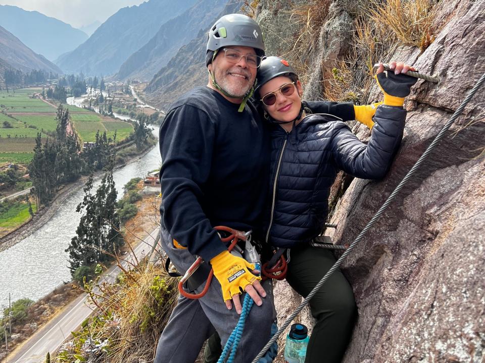 Victoria and her dad smile for a picture while climbing via ferrata on the side of a cliff.