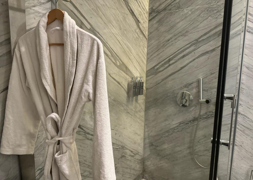 A bathrobe hanging outside a marble shower stall .