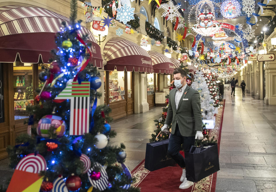 FILE - In this Monday, Nov. 23, 2020 file photo, a man wearing face mask and gloves to protect against coronavirus carries purchases among as the GUM State Department store is decorated for Christmas and New Year celebrations in Moscow, Russia. Nations are struggling to reconcile cold medical advice with a holiday tradition that calls for big gatherings in often poorly ventilated rooms, where people chat, shout and sing together, providing an ideal conduit for a virus that has killed over 350,000 people in Europe so far. (AP Photo/Pavel Golovkin, File)