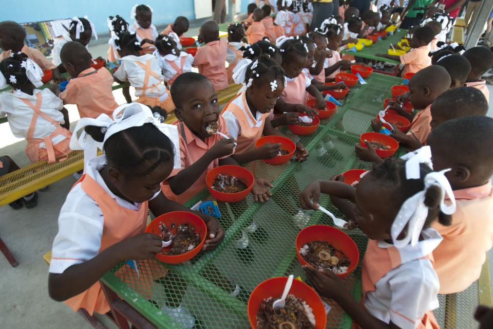 Children of the Union Des Apotres – Prodev School eat after the visit of Former U.S. President and UN special envoy to Haiti Bill Clinton in Cite Soleil, Port-au-Prince, Haiti, Monday Feb. 17, 2014. Clinton is in Haiti to visit several projects that focus on agriculture and the environment, including the Union Des Apotres – Prodev solar-powered school that his private foundation has assisted and a training school for Haitian coffee farmers. (AP Photo/Dieu Nalio Chery)