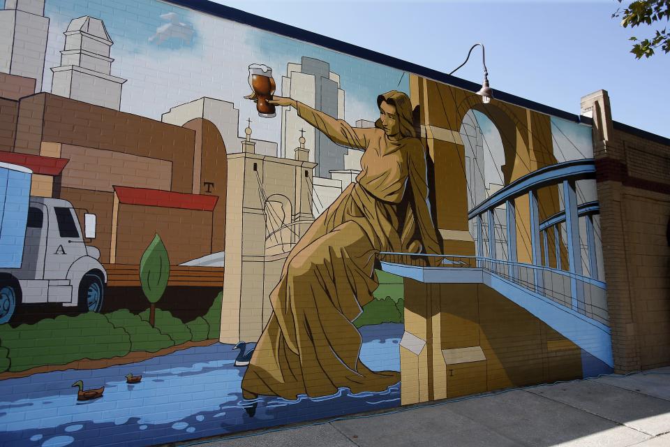From 2015: Tyler Davidson's "Genius of Water" is perched on the Roebling Bridge while raising her glass. The Sam Adams Brewery unveiled a mural facing Central Parkway, depicting the community's significant history and vibrant future. Cincinnati artist and designer Tom Post was commissioned to create the mural depicting the values of Samuel Adams beer, Cincinnati's brewing heritage and Over-the-Rhine's rich brewing culture.