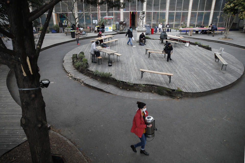 A volunteer carries a tea distribution machine in the "Aurore" center for homeless and migrants in Paris, Thursday, April 2, 2020. Amid the coronavirus lockdown, charity workers at France's Aurore association, are preparing more than a thousand meals a day for migrants and the homeless on the half-abandoned grounds of a former Paris hospital whose patron saint was devoted to the poor. (AP Photo/Francois Mori)