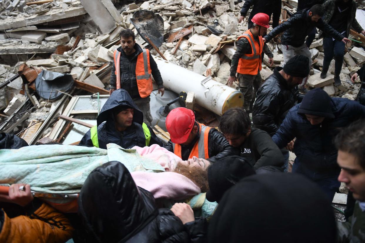 Syrian civil defence members carry an injured woman after rescuing her from the rubble of a collapsed building (AFP via Getty Images)