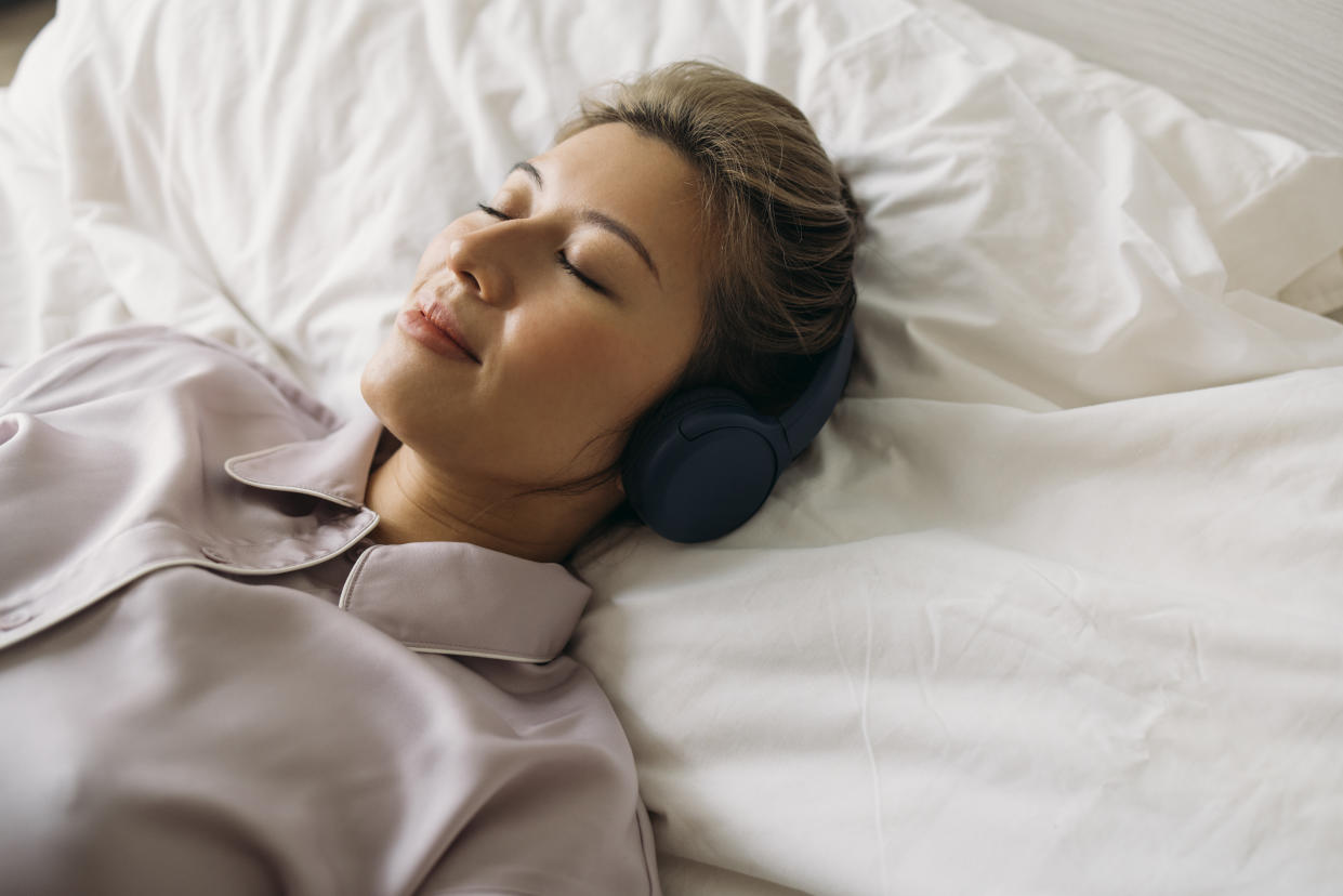 A from above view of a happy Asian female in pajamas napping peacefully with  headphones on her head.