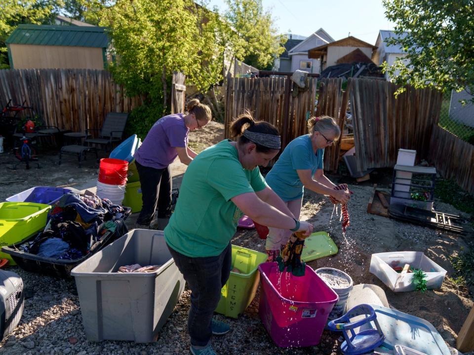 three women ring out clothing over plastic bins outside