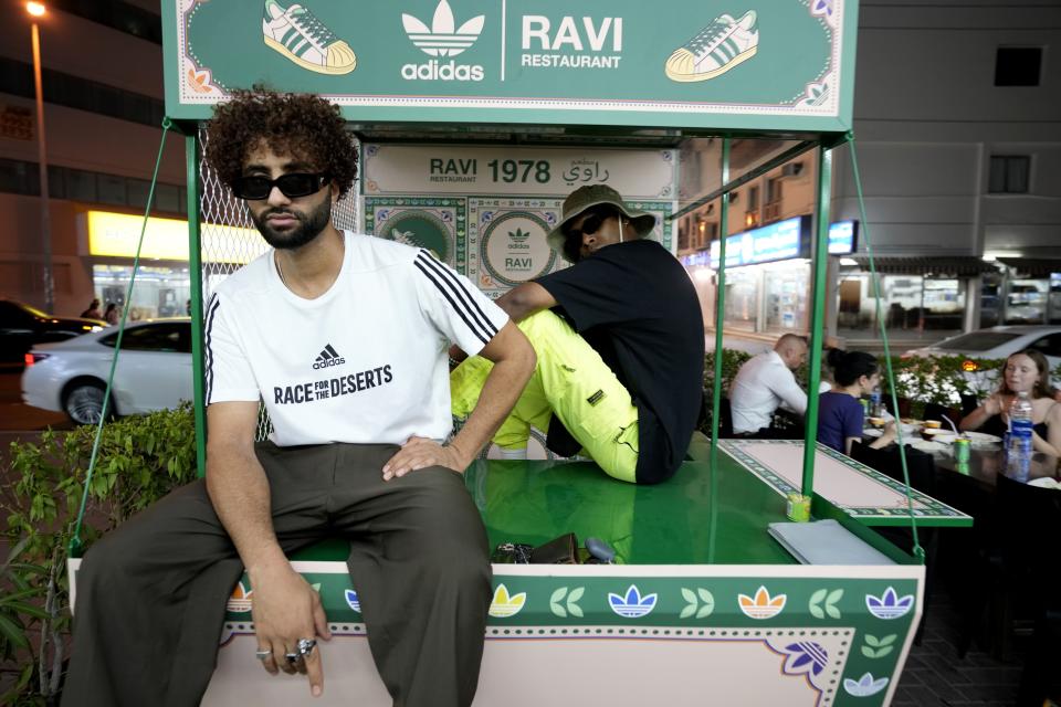 People pose for photos with Ravi X Adidas truck in front of the Ravi restaurant in Satwa district of Dubai, United Arab Emirates, Wednesday, June 22, 2022. Adidas has teamed up with Dubai nostalgic family-owned Pakistani restaurant to release the Superstar Ravi sneaker. (AP Photo/Kamran Jebreili)