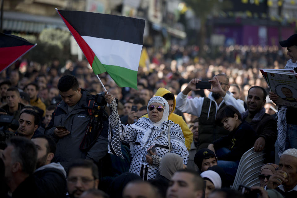 A Palestinian Fatah supporter dressed in keffiyehs waves a Palestinian flag during a celebration marking the 55th anniversary of the Fatah movement, in the West Bank city of Ramallah, Tuesday, Dec. 31, 2019. (AP Photo/Majdi Mohammed)